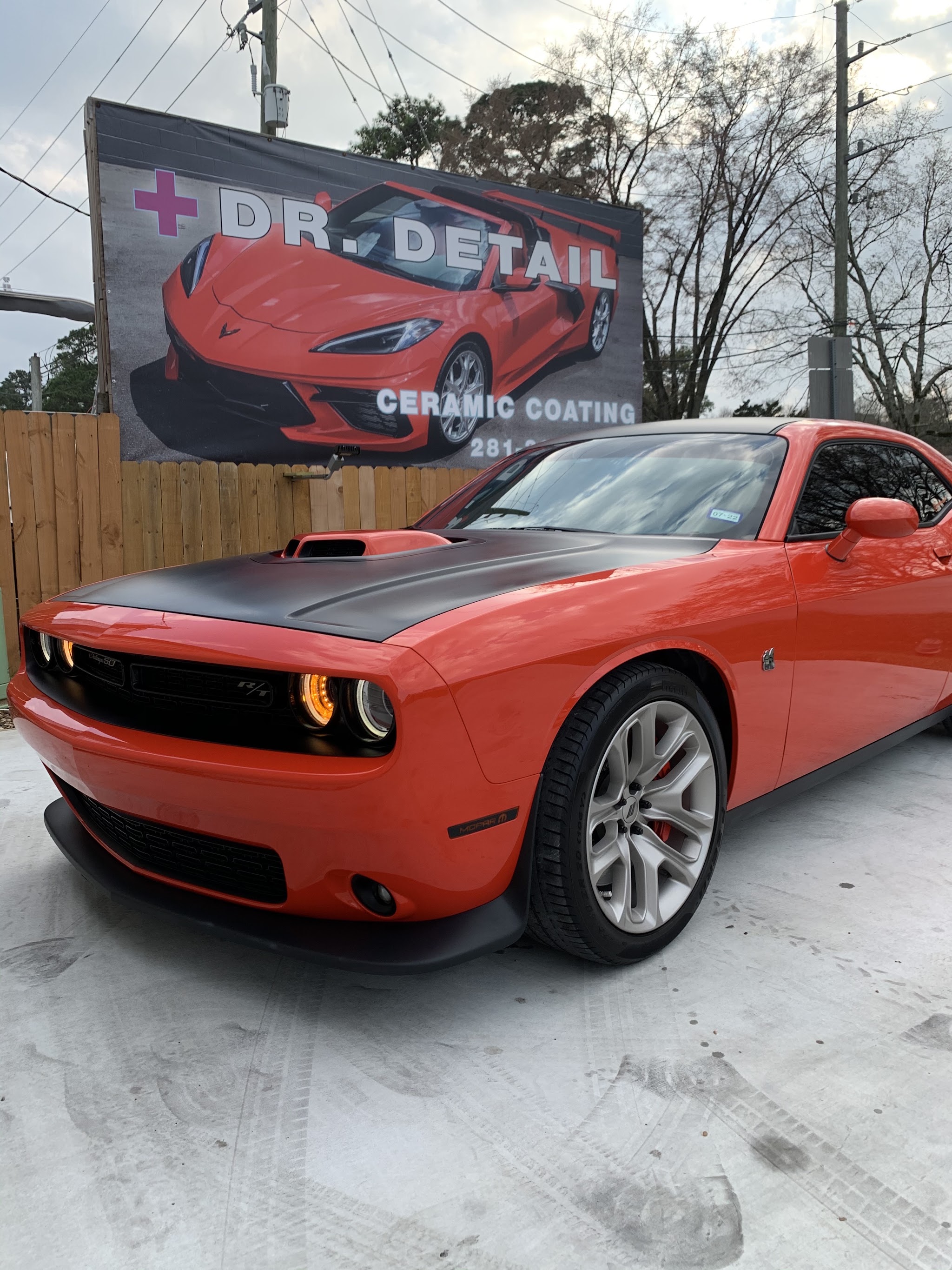 An orange Dodge Challenger in front of the Dr. Detail ceramic coating billboard