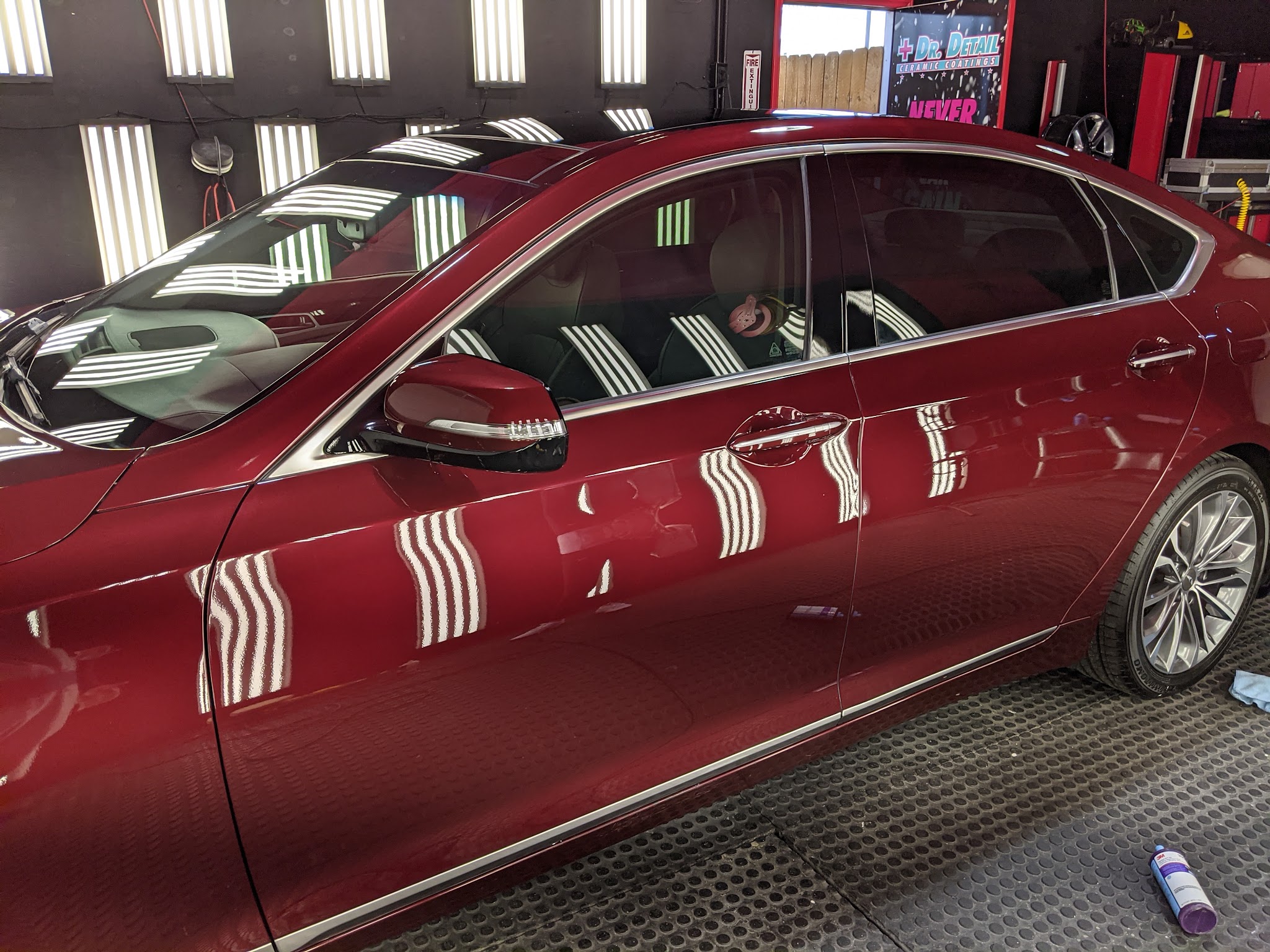 A deep red sedan in the Dr. Detail bay, the LED wall panels reflected as clean stripes along its doors
