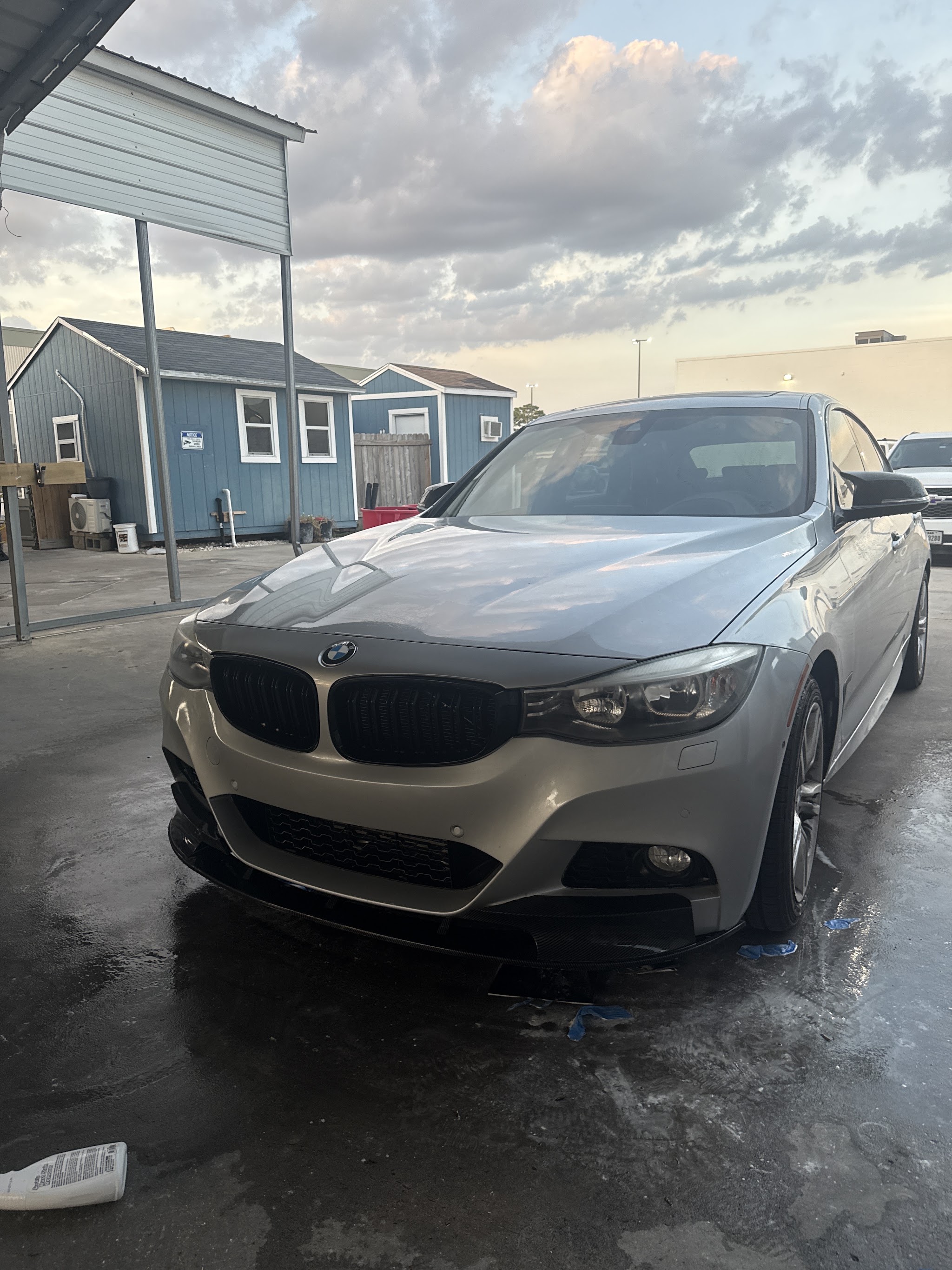 A silver BMW on the wet wash pad under the canopy at dusk