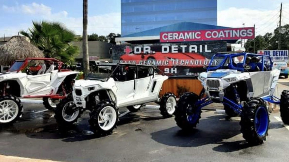 Three UTVs lined up in front of the Dr. Detail ceramic coatings roadside sign