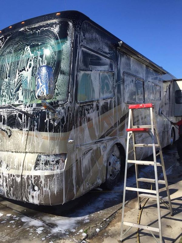 A motorhome covered in wash foam beside a ladder