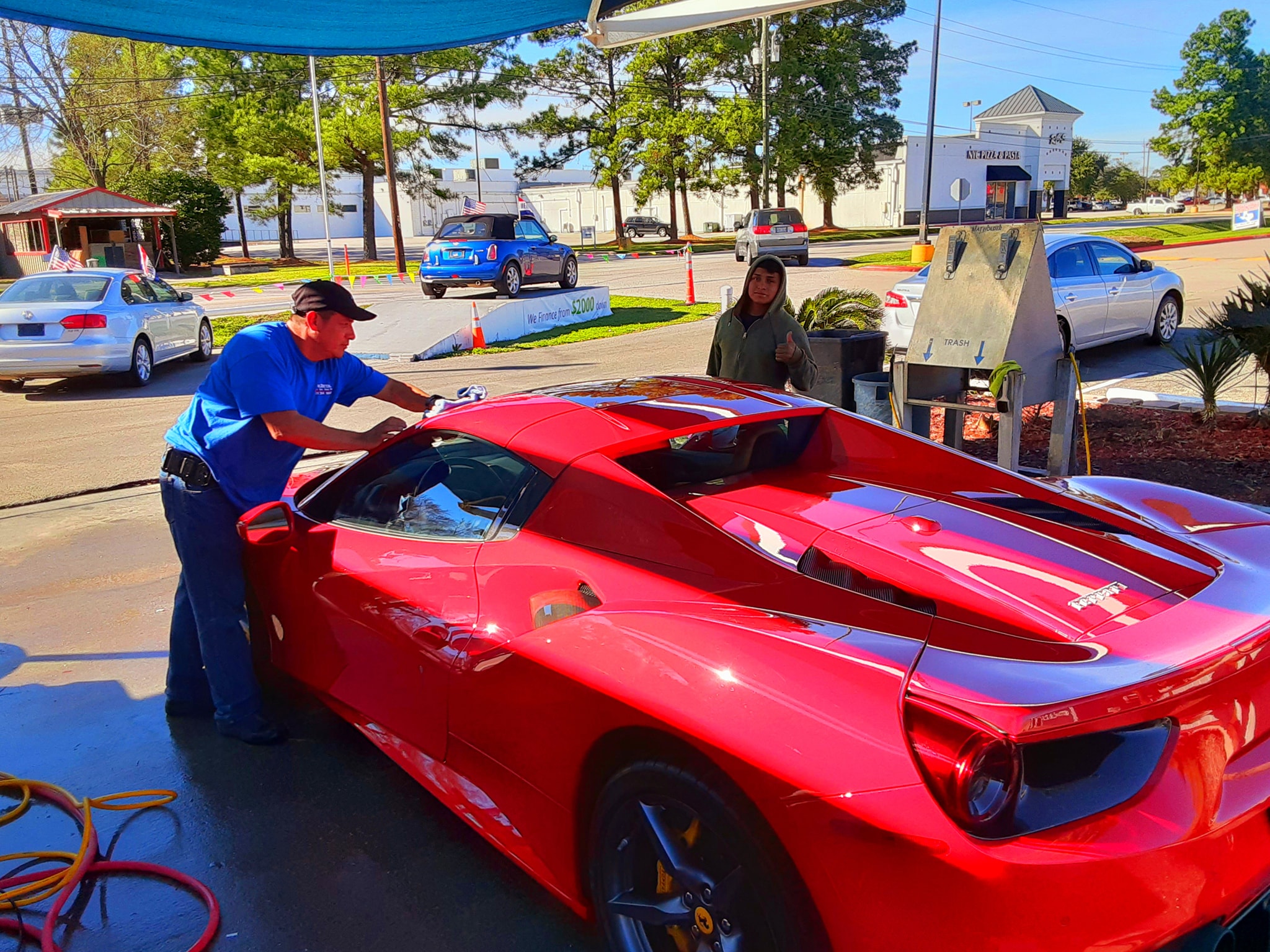 A Dr. Detail team member hand-drying a red Ferrari under the wash-pad canopy